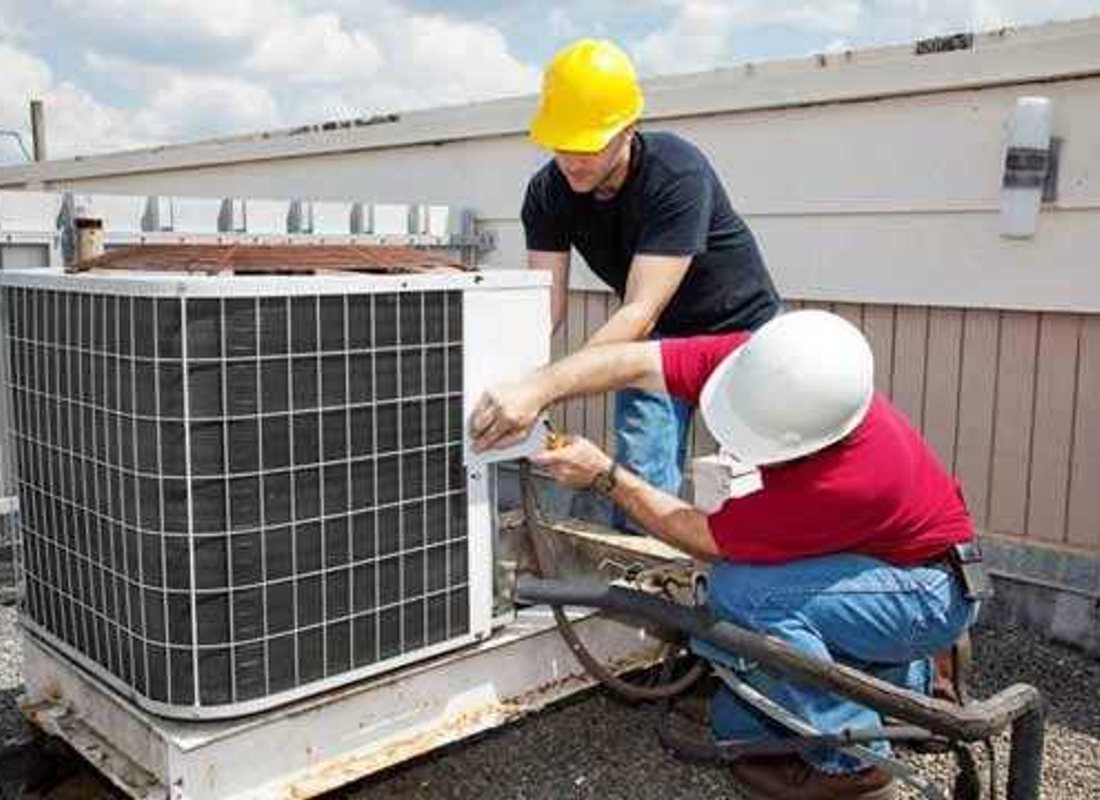 Two HVAC technicians working on an outdoor air-conditioning unit beside a brick home